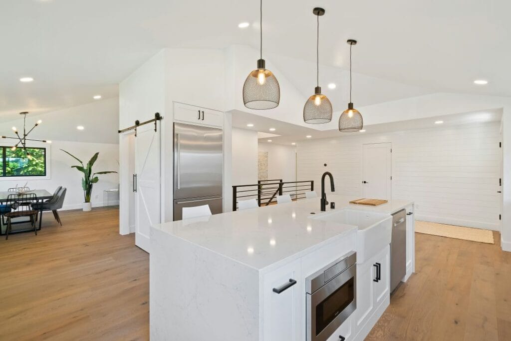 Spacious White Kitchen with Wooden Floors and Modern Light Fixtures